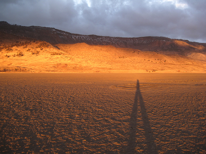 Artist Dawn Chandler's shadow walking across the playa at sunrise. Playa in Summer Lake, Oregon