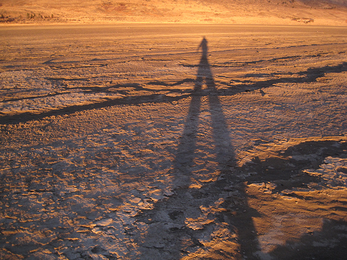 Artist Dawn Chandler's shadow walking across the playa at sunrise. Playa in Summer Lake, Oregon