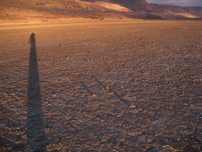 Artist Dawn Chandler's shadow pausing on the playa at sunrise. Playa in Summer Lake, Oregon