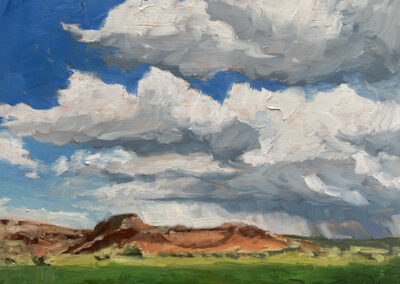 New Mexico landscape painting by artist Dawn Chandler of Ghost Ranch after the rain, with distant red and ochre cliffs rising above vivid green fields under towering blue‑gray storm clouds and bright white cumulus clouds breaking open to patches of blue sky