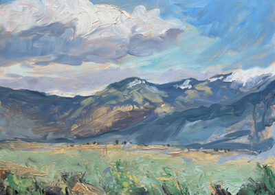 Spring morning New Mexico landscape painting of the Taos Mountains by artist Dawn Chandler, with snow‑tipped blue peaks under sweeping clouds above a sunlit green and gold valley in loose, textured brushstrokes.